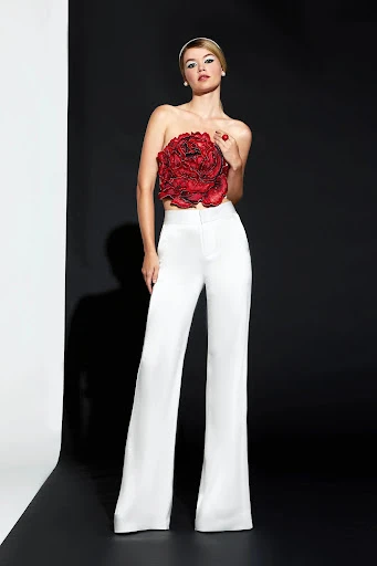 Full-length shot of a woman in white pants and a large floral top, posing against a black and white background in a studio.