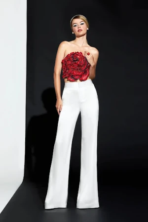 Full-length shot of a woman in white pants and a large floral top, posing against a black and white background in a studio.
