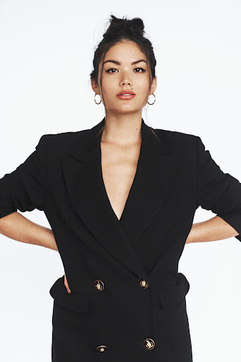 Portrait of an Asian adult female wearing a black blazer-style dress with gold buttons against a plain white background.