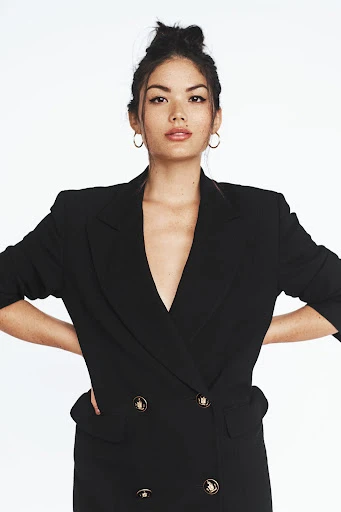Portrait of an Asian adult female wearing a black blazer-style dress with gold buttons against a plain white background.