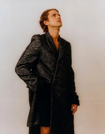 Man wearing a dark textured tweed coat looking upward against a plain neutral background