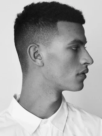 Profile portrait of a young man with short dark hair wearing a white collared shirt against a plain light background