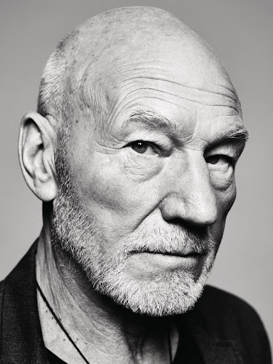 Close-up monochrome portrait of Patrick Stewart with a serious expression against a grey background.