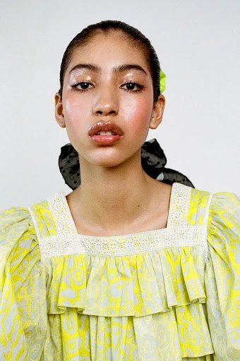 Portrait of a young woman with glossy lips and a yellow ruffled dress against a white background. Beauty and fashion headshot.