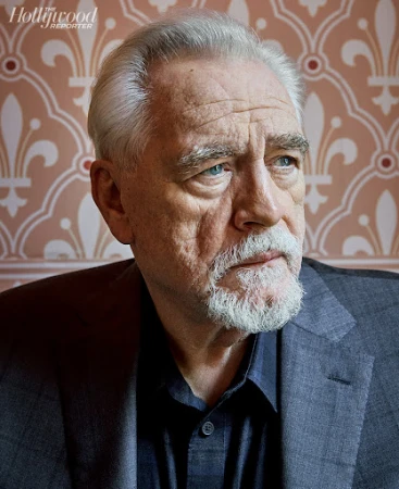Headshot of older male actor with gray hair and beard in dark blazer against patterned wallpaper for The Hollywood Reporter.