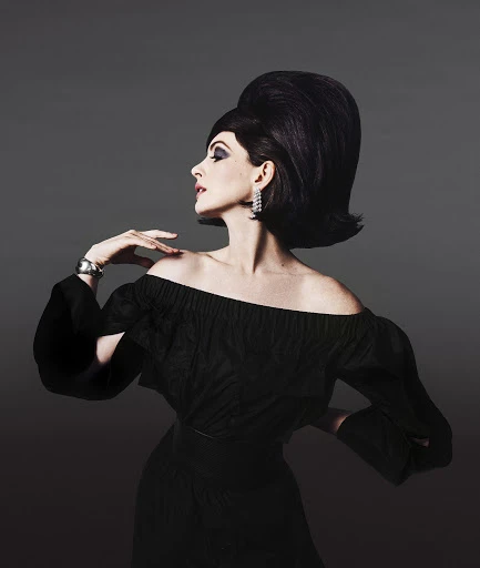 Elegant woman with bouffant hairstyle, off-shoulder black dress, silver bracelet, and diamond earrings poses against a gray backdrop.