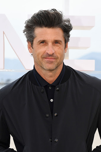 Portrait of actor Patrick Dempsey in black bomber jacket against blurred outdoor backdrop at event, showcasing casual celebrity style.