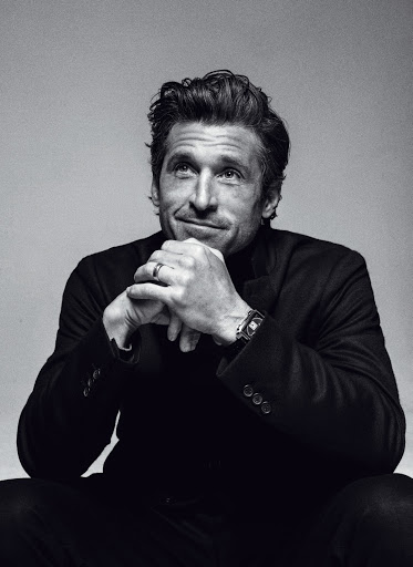 Black and white portrait of an adult male with dark hair wearing a black suit jacket and turtleneck, looking off-camera.