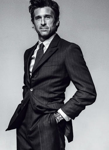 Black and white portrait of an adult male wearing a suit and tie, posing with one hand in his pocket against a plain background.
