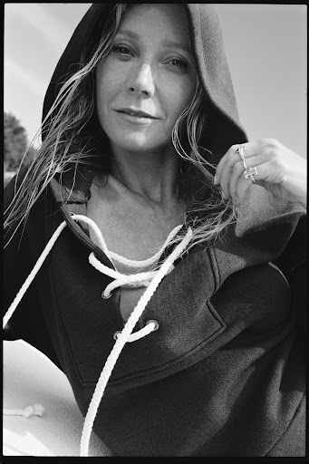 Black and white portrait of a woman with long hair wearing a hoodie with laces, looking at the camera with a slight smile.
