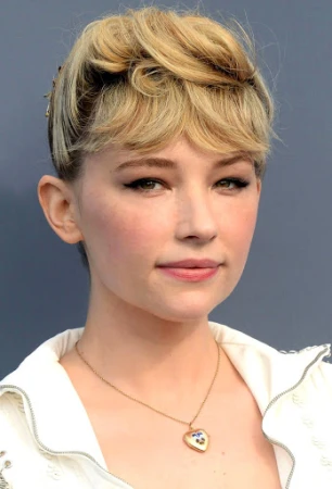 Portrait of Haley Bennett with blonde pinned-up hair, winged eyeliner, and a heart locket necklace against a grey backdrop.