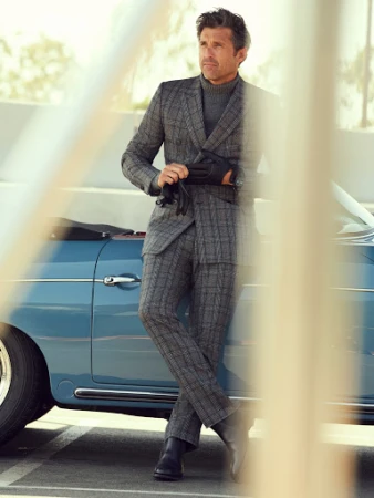Adult male in a grey plaid suit poses next to a vintage blue convertible car in a stylish outdoor automotive fashion shot.