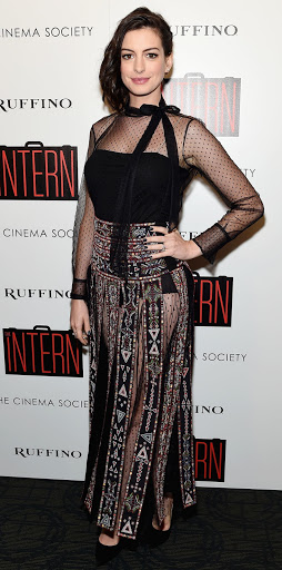 Anne Hathaway poses on a red carpet at an event for her movie, 'The Intern', wearing a long, black dress with geometric patterns.