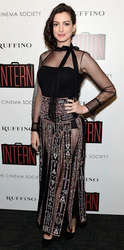 Anne Hathaway poses on a red carpet at an event for her movie, 'The Intern', wearing a long, black dress with geometric patterns.