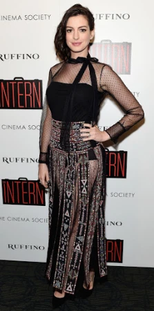 Anne Hathaway poses on a red carpet at an event for her movie, 'The Intern', wearing a long, black dress with geometric patterns.