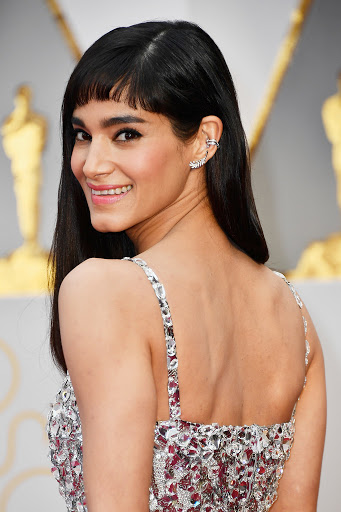 Portrait of Sofia Boutella on red carpet wearing a sparkling silver dress and diamond jewelry, smiling at the camera at a premiere.