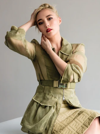 Woman in an olive green mesh jacket and matching belted skirt posing against a neutral grey studio backdrop
