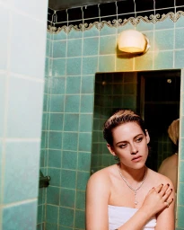 Kristen Stewart wearing a white towel and diamond necklace in a turquoise tiled bathroom with makeup by Jillian Dempsey