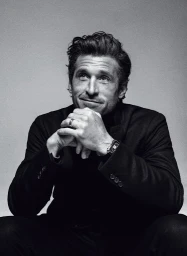 Monochrome portrait of Patrick Dempsey resting his chin on clasped hands with a thoughtful expression