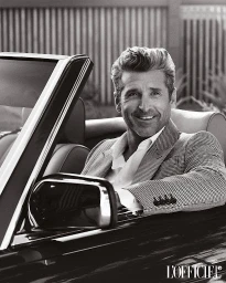 Patrick Dempsey smiling in a convertible car wearing a patterned blazer and white shirt in a black and white portrait.