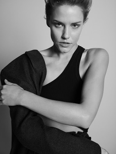 Black and white portrait of a woman wearing a black tank top and dark jacket against a plain background.