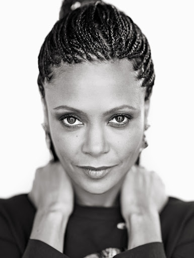 Black and white portrait of a woman with braided hair, wearing a dark top, with her hands near her neck, against a white background.
