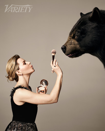 Profile of an adult female holding a makeup brush and compact opposite a bear head against a neutral backdrop for Variety.