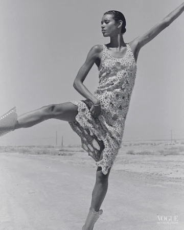 Woman in patterned dress and studded boots strikes a ballet pose in black and white on an outdoor barren landscape with clear sky.