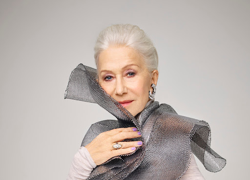 Portrait of mature woman with silver hair wearing modern metallic collar, statement earrings, and ring posing in studio on neutral background.