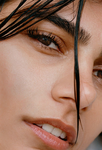 Close-up beauty portrait of a woman's face with wet dark hair strands falling across her forehead and eyes.