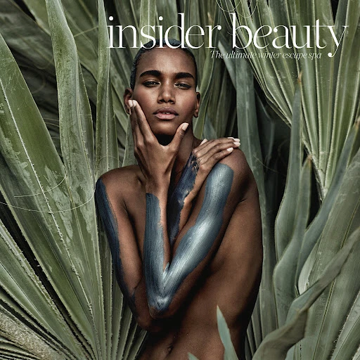 Beauty editorial featuring a bare-shouldered woman with clay on her arms, posing in front of green tropical foliage. Insider Beauty magazine cover.