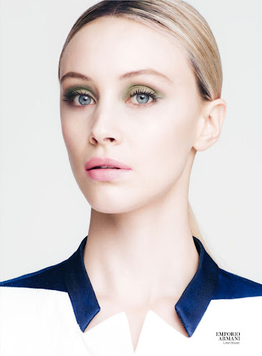 Close-up fashion beauty shot of a fair-skinned adult female model with green eye shadow and light pink lipstick, wearing a dress with a blue collar.