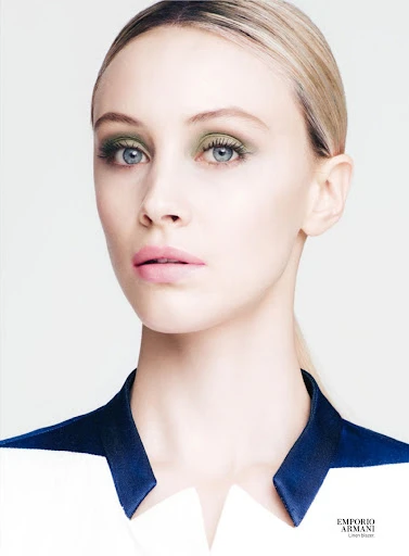 Close-up fashion beauty shot of a fair-skinned adult female model with green eye shadow and light pink lipstick, wearing a dress with a blue collar.