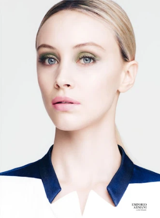 Close-up fashion beauty shot of a fair-skinned adult female model with green eye shadow and light pink lipstick, wearing a dress with a blue collar.