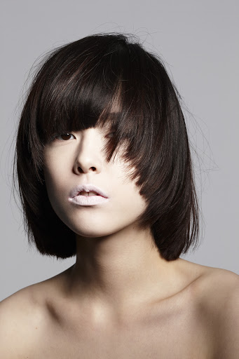 Headshot of a young adult woman with dark, short hair, light skin, and pale pink lipstick, posing in a photo studio with a grey background.