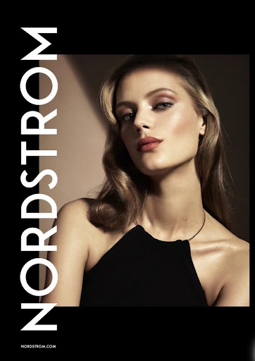 Close-up portrait of a woman wearing a black halter top with makeup by Lisa Houghton against a dark background.