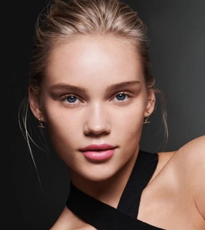 Close-up portrait of a woman with blonde hair, pink lipstick, and a black halter strap against a dark background.