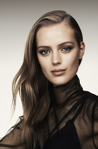 Close-up studio portrait of a fair-skinned adult woman with long wavy brown hair, wearing a black mesh top and makeup.