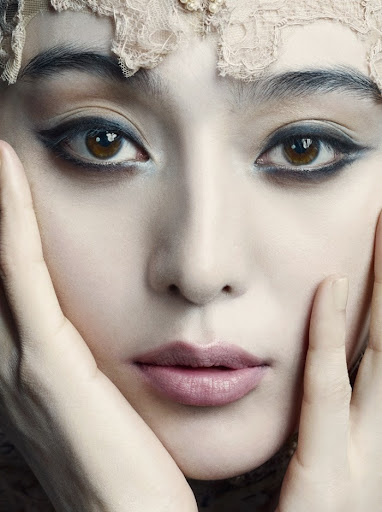 Close-up portrait of an adult woman with fair skin, dramatic eyeliner and light pink lipstick, with hands near her face.