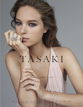 Close-up portrait of a woman wearing diamond rings and a delicate necklace against a plain grey background with overlay text.