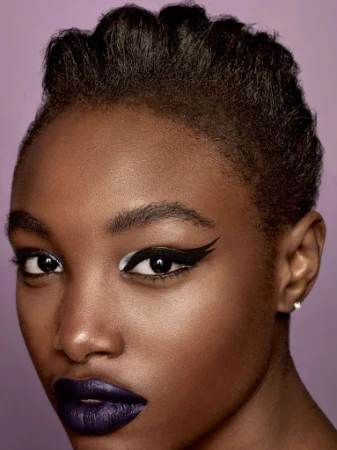 Close-up beauty portrait of a Black woman with bold graphic winged eyeliner and dark purple lipstick by makeup artist Lisa Houghton