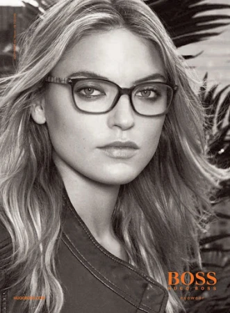Monochrome portrait of a blonde woman wearing square-framed glasses, a dark jacket, and a neutral expression, in a Boss eyewear ad.