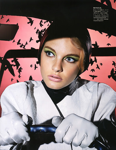 Close-up of a woman wearing light eye makeup and gloves, holding a steering wheel, with a red background and bird silhouettes.