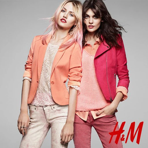 Two fashion models pose in front of a gray background, wearing coordinated outfits with jackets, tops, and colored jeans.