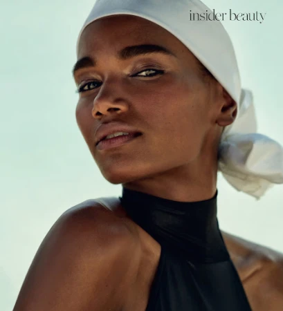 Close-up beauty portrait of a woman wearing a white headscarf and black halter top against a pale sky background