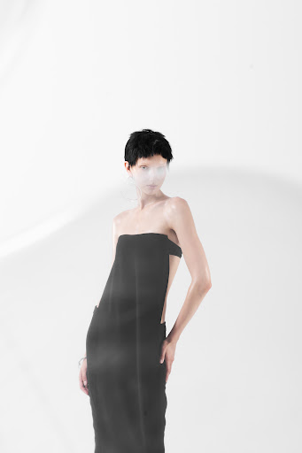 Model with short dark hair wearing a strapless black dress against a white studio background