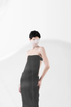 Model with short dark hair wearing a strapless black dress against a white studio background