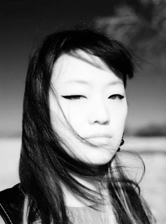 Close-up monochrome portrait of a woman with long dark hair blowing across her face and dramatic winged eyeliner.