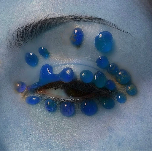 Macro close-up of woman's eye with vivid blue makeup and decorative gel beads for a surreal, artistic beauty statement and creative aesthetic.