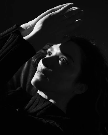 Monochrome portrait of a woman with hands raised, face lit from below, in black and white with high contrast.